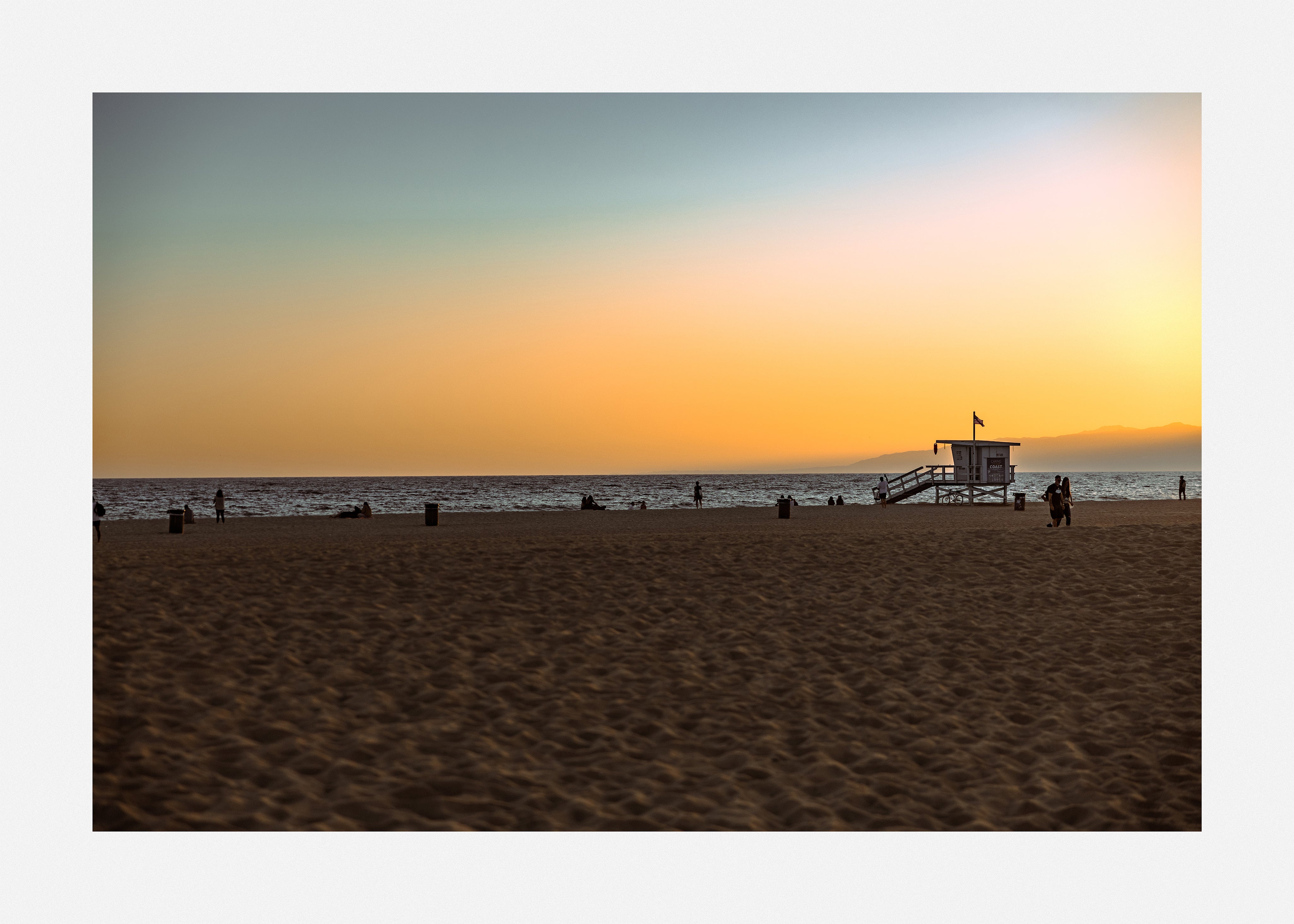 Photography art print of golden light reflecting off gentle waves on a sandy beach.